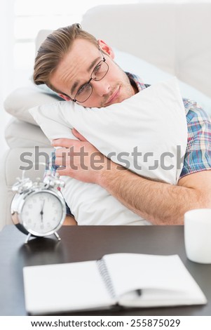 Bored man beside alarm clock hugging a pillow at home in the living room