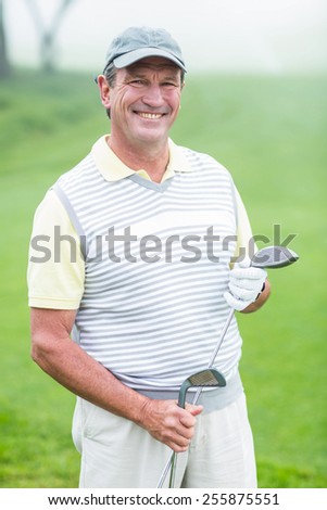 Cheerful golfer smiling at camera holding his club on a foggy day at the golf course