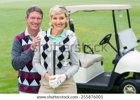 Happy golfing couple with golf buggy behind on a foggy day at the golf course