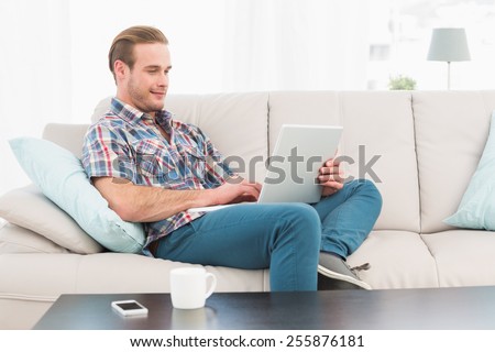 Relaxed man sitting on sofa using laptop at home in the living room