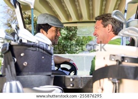 Golfing friends driving in their golf buggy smiling to each other at golf course