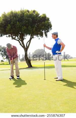 Golfer swinging his club with friend at the golf course