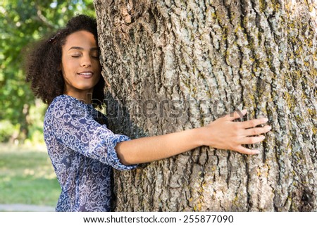 Pretty young woman hugging a tree on a summers day