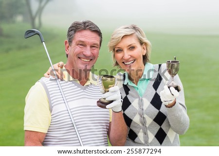 Happy golfing couple with trophy on a foggy day at the golf course