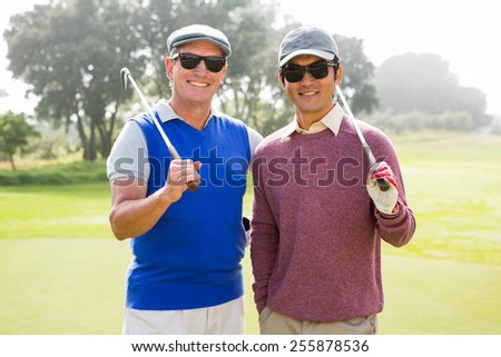 Golfing friends smiling at camera holding clubs at the golf course