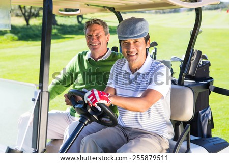 Golfing friends driving in their golf buggy smiling at camera at the golf course