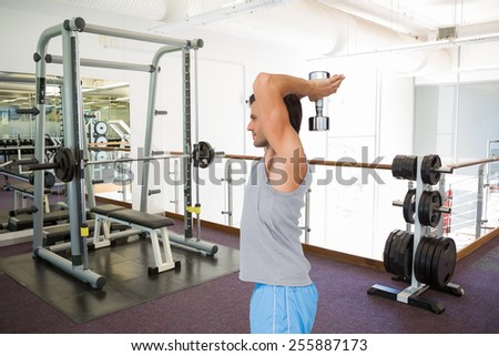 Side view of a fit man exercising with dumbbell against empty weights room with bench press