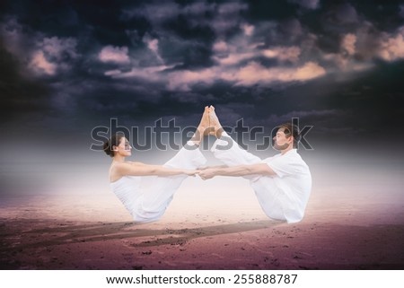 Peaceful couple sitting in boat position together against dark cloudy sky