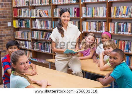 Cute pupils and teacher reading in library at the elementary school