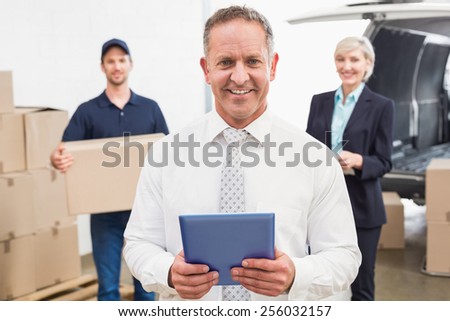 Smiling manager holding tablet in front of his colleagues in a large warehouse