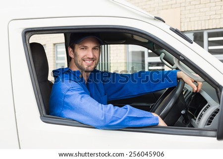 Delivery driver smiling at camera in his van outside the warehouse