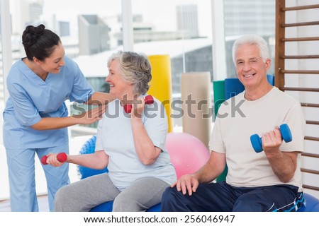 Happy trainer communicating with senior woman sitting by man in gym