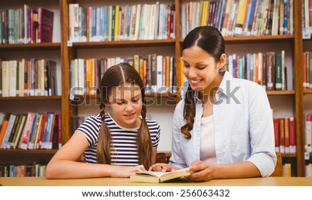 Female teacher and little girl reading book in the library