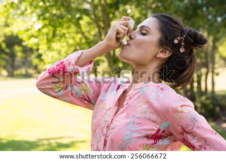Pretty brunette using her inhaler on a summers day