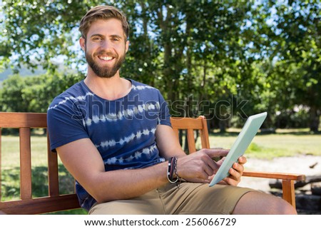 Young man using tablet on park bench on a summers day