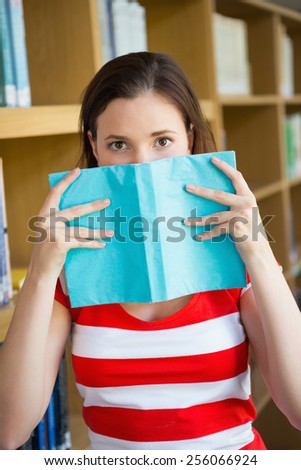 Student covering face with book in library at the university
