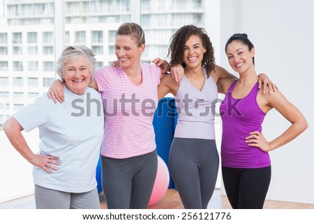 Portrait of happy female friends standing arms around in fitness studio