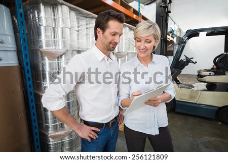 Smiling warehouse managers with clipboard in a large warehouse