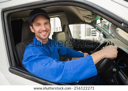 Delivery driver smiling at camera in his van outside the warehouse