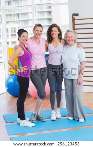 Full length portrait of happy women standing arms around in gym