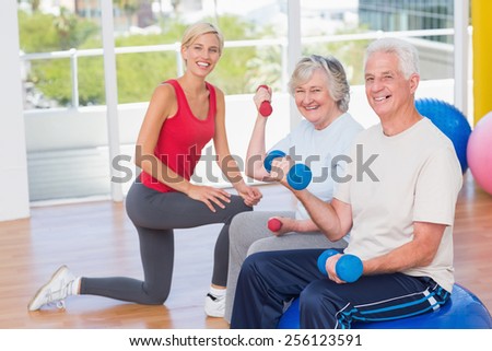 Portrait of happy senior couple lifting dumbbells by trainer in gym