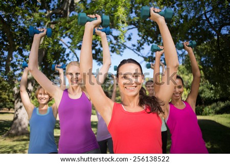 Fitness group lifting hand weights in park on a sunny day