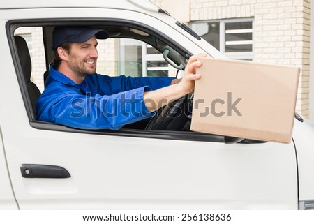 Delivery driver offering parcel from his van outside the warehouse