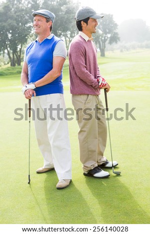 Golfing friends smiling and holding clubs at golf course