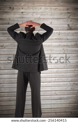 Businessman standing back to the camera with hands on head against wooden planks background