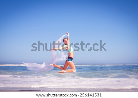 Fit woman jumping gracefully on the beach with scarf against fitness interface