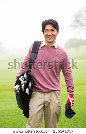 Golfer standing holding his golf bag smiling at camera at the golf course