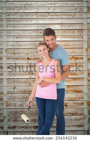 Young couple painting with roller against wooden background in pale wood