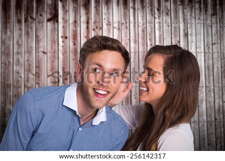 Happy young woman whispering secret into friends ear against wooden planks