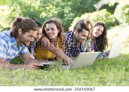 Smiling friends in the park using tablet pc and laptop on a sunny day
