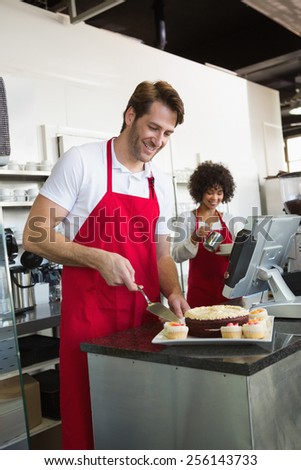 Smiling waiter slicing cake with waitress behind him at the bakery