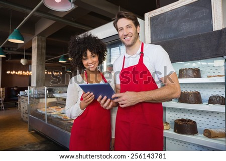 Happy co-workers in red apron holding tablet at the bakery