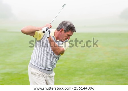 Golfer swinging his club on the course on a foggy day at the golf course
