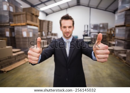 Warehouse manager smiling at camera showing thumbs up in a large warehouse