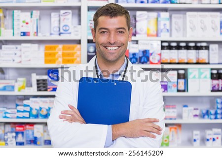Happy pharmacist holding clipboard at the hospital pharmacy
