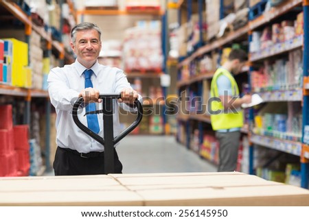 Manager pulling trolley with boxes in front of his employee in warehouse
