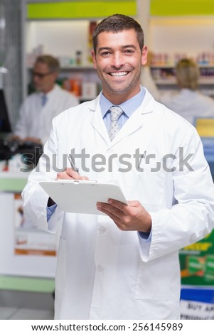 Happy pharmacist writing on clipboard at the hospital pharmacy