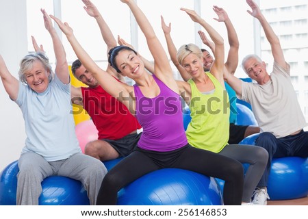 Portrait of happy men and women on fitness balls exercising in gym class