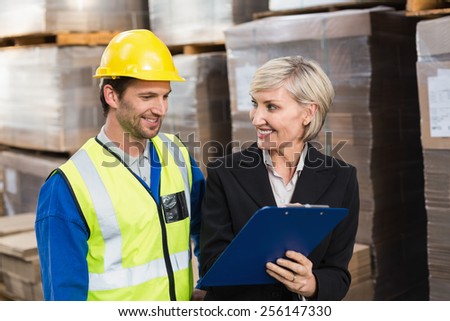Warehouse manager showing clipboard to her colleague in a large warehouse
