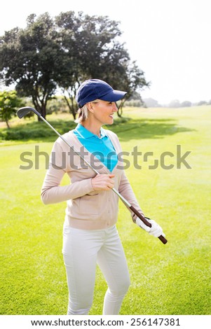 Female golfer standing holding her club smiling on a sunny day at the golf course