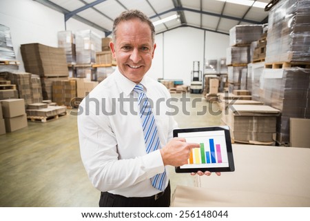Smiling boss showing column graphic on the tablet in a large warehouse