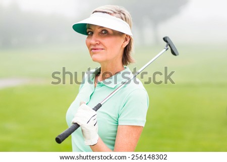 Golfer standing and swinging her club smiling at camera on a foggy day at the golf course