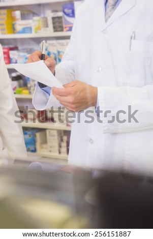 Mid section of pharmacist writing a prescription in the pharmacy