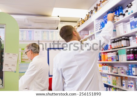 Pharmacist in lab coat taking jar from shelf in the pharmacy