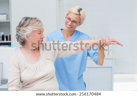 Happy female nurse assisting senior patient in exercising at clinic