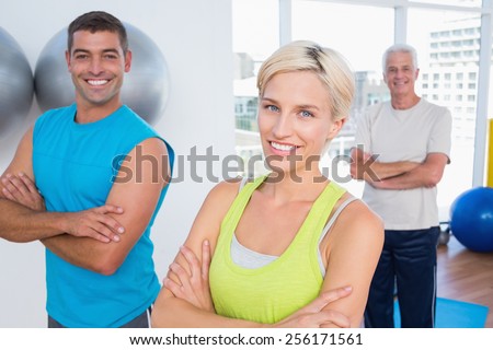 Portrait of happy woman with male friends standing arms crossed at gym class